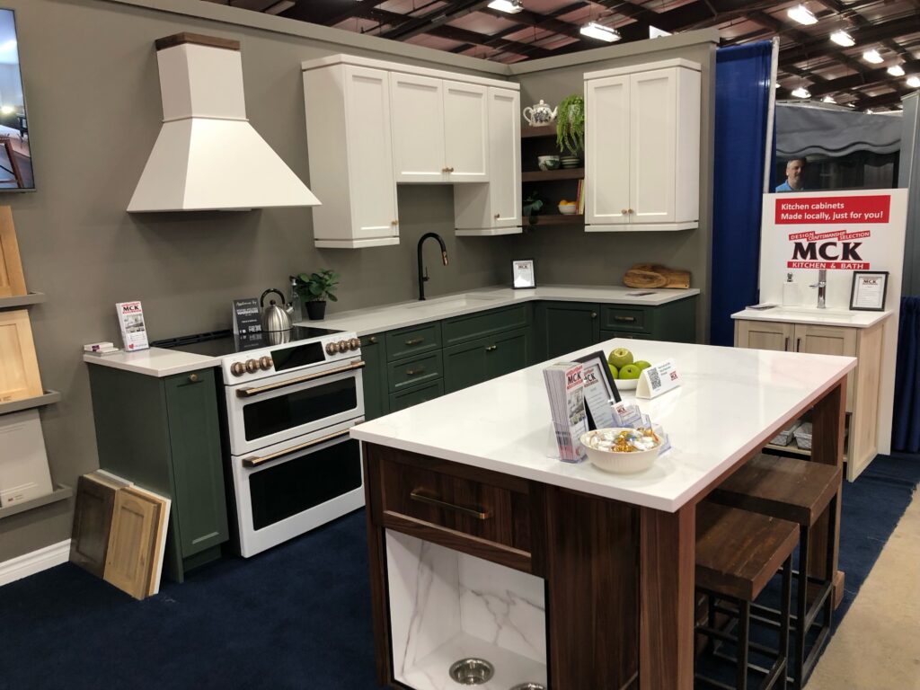 2024 Ideal Home Show booth. Forest green shaker kitchen with dove white uppers. Natural walnut island with pet feeding station.